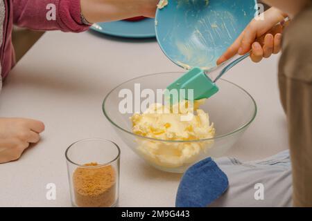 Kinder mit ihrer Mutter, die einen Kuchen zubereiten und die Zutaten Butter im Vordergrund mischen Stockfoto