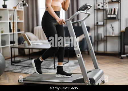 Zugeschnittener Blick auf Hände und Beine einer jungen, sportlichen afrikanerin, die morgens im Fitnessstudio mit dem Laufband trainiert. Konzept von Sport, Aktivität, gesundem Lebensstil. Stockfoto