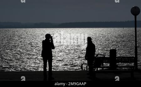 Rerik, Deutschland. 18. Januar 2023. Das Wasser auf der Salzhaff scheint in die Sonne, Spaziergänger sind draußen am Hafen. Im Norden dominiert ruhiges und teilweise sonniges Wetter. Kredit: Bernd Wüstneck/dpa/Alamy Live News Stockfoto