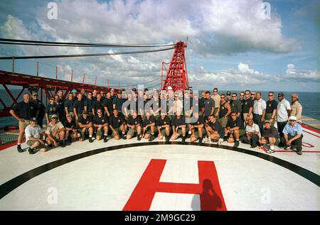 Mitglieder der Crew der National Oceanic and Atmospheric Administration (NOAA) und der US Navy (USN) Taucher, die der mobilen Taucher- und Bergungseinheit zwei (MDSU-2) zugeteilt sind, versammeln sich während der Phase II der Monitor 2001 Expedition auf dem Hubschrauberlandeplatz des Derrick Barge WOTAN für ein Gruppenfoto. Basis: Mason-Gulf Derrick Barge Wotan Stockfoto