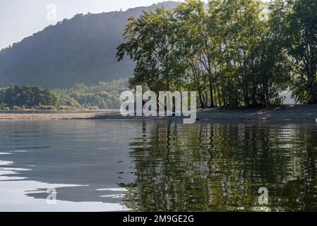 Ein Kanufahrer, der eine kleine Insel mit Bäumen erkundet, die sich in der Oberfläche des Lake Windermere, Cumbria, England, spiegeln Stockfoto