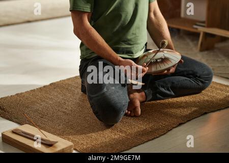 Nahaufnahme eines Yoga-Mannes, der in Lotusposition auf Teppich sitzt und Fimbo in seiner Praxis benutzt Stockfoto