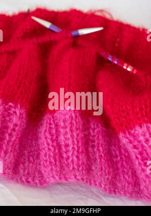 Handgestrickter Pullover aus pinkfarbenem und rotem Mohair-Garn mit Stickerei und Rippnähten, gestrickt auf runden Nadeln. Stockfoto
