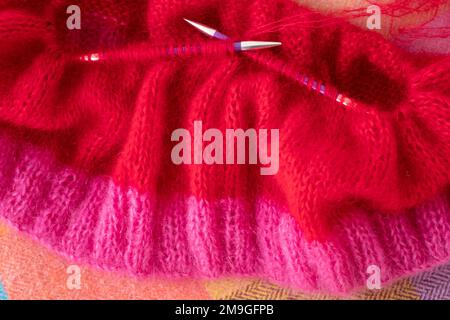 Handgestrickter Pullover aus pinkfarbenem und rotem Mohair-Garn mit Stickerei und Rippnähten, gestrickt auf runden Nadeln. Stockfoto