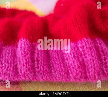 Handgestrickter Pullover aus pinkfarbenem und rotem Mohair-Garn mit Stickerei und Rippnähten, gestrickt auf runden Nadeln. Stockfoto