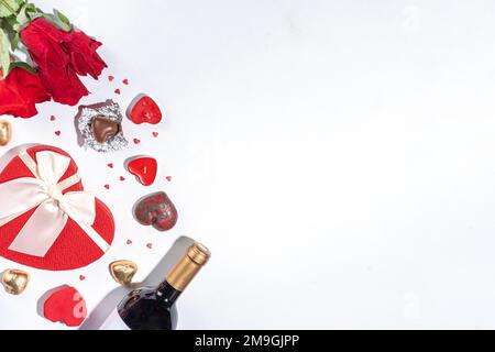 Grußkarte zum Valentinstag flach gelegt. Einsamer weißer Hintergrund am Valentinstag mit Weinflasche, süßen Schokolade, Strauß roter Rosen, Geschenk Stockfoto