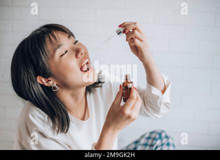 Eine Asiatin tropft cbd-Öl in den Mund. Nahaufnahme asiatischer Frauen, die CBD-Öl zum Schlafen nehmen. Medizinisches Cannabis. Vitamine und Nahrungsergänzungsmittel Stockfoto