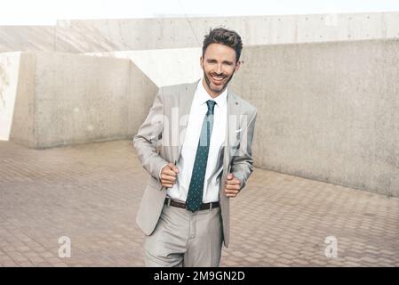 Ein junger, attraktiver lächelnder Geschäftsmann steht neben einer Betonwand und trägt einen hellen klassischen Smoking. Arbeitsstil im Stadtverkehr. Stockfoto