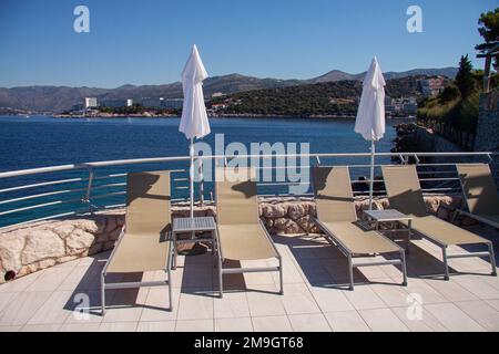 Leere Sonnenliegen in einer Reihe im Erholungsbereich am blauen Meer und einem Swimmingpool. Mit abgesenkten weißen Sonnenschirmen und blauem Himmel. Dubrovnik, Kroatien - Jul Stockfoto