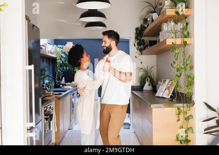 Ein birassisches junges Paar, das sich ansieht, während es nachts romantisch in der Küche tanzt Stockfoto