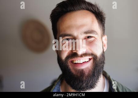 Nahaufnahme eines hübschen bärtigen, birassischen jungen Mannes, der an der weißen Wand lächelt, Kopierraum Stockfoto