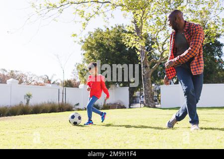 Glücklicher afroamerikanischer Vater und Sohn, die im Garten Fußball spielen Stockfoto