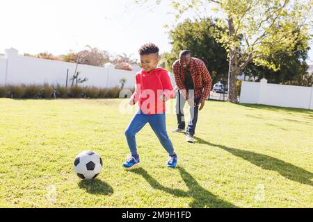 Glücklicher afroamerikanischer Vater und Sohn, die im Garten Fußball spielen Stockfoto