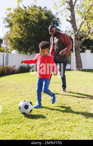Glücklicher afroamerikanischer Vater und Sohn, die im Garten Fußball spielen Stockfoto