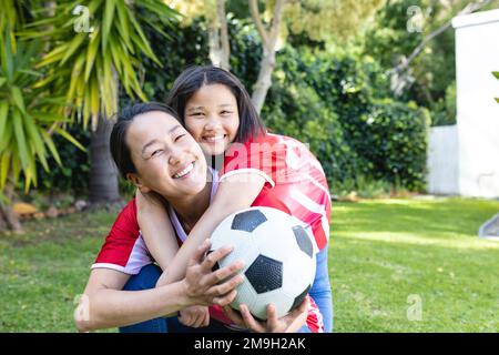 Porträt einer glücklichen asiatischen Mutter und Tochter, die zusammen im Garten Fußball spielen Stockfoto