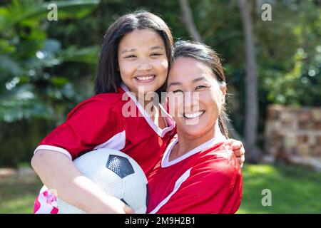 Porträt einer glücklichen asiatischen Mutter und Tochter, die zusammen im Garten Fußball spielen Stockfoto