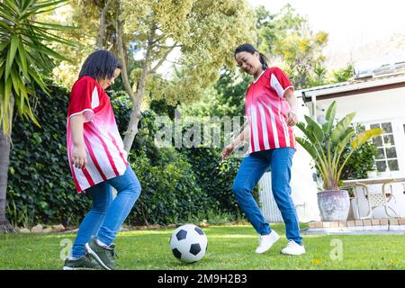 Glückliche asiatische Mutter und Tochter, die zusammen im Garten Fußball spielen Stockfoto