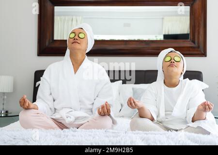 Glückliche asiatische Mutter und Tochter sitzen auf dem Bett und meditieren Stockfoto