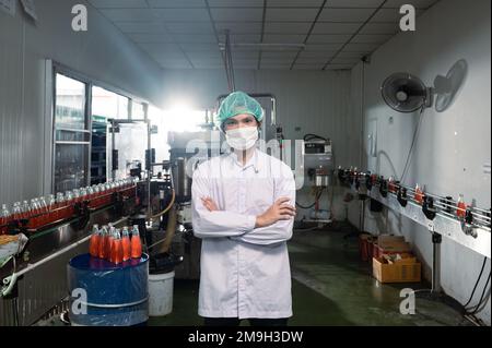 Selbstbewusster asiatischer Vorgesetzter im Sterilanzug mit Flaschenproduktionslinie in einer Getränkefabrik Stockfoto