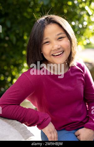 Porträt eines glücklichen asiatischen Mädchens, das in die Kamera schaut und im Garten lächelt Stockfoto