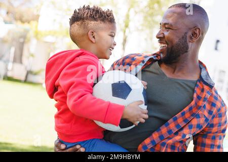 Glücklicher afroamerikanischer Vater und Sohn, die im Garten Fußball spielen Stockfoto