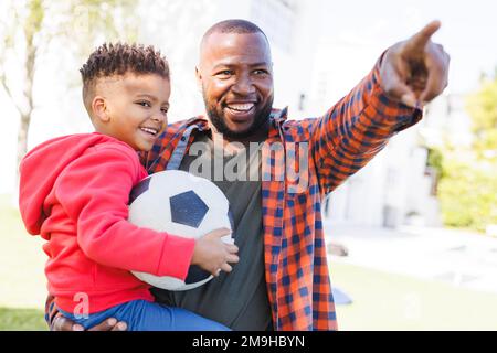 Glücklicher afroamerikanischer Vater und Sohn, die im Garten Fußball spielen Stockfoto