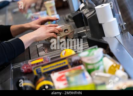 Neubiberg, Deutschland. 18. Januar 2023. Ein Kassierer scannt Produkte an der Kasse in einem Supermarkt. Angesichts der hohen Inflation erwarten die Verbraucherverbände einen weiteren Anstieg der Lebensmittelpreise. Kredit: Sven Hoppe/dpa/Alamy Live News Stockfoto