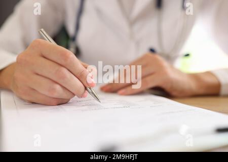 Eine Ärztin füllt medizinische Formulare aus, während sie an ihrem Schreibtisch in der Klinik sitzt. Stockfoto