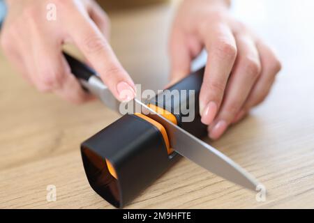 Frauenhände schärfen Messer mit Spitzer auf Küchentisch Nahaufnahme. Stockfoto