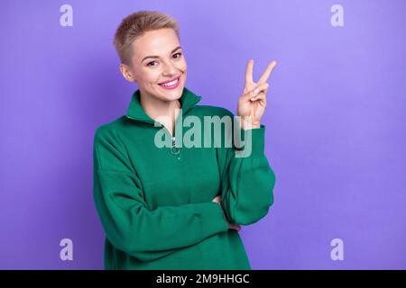 Foto eines positiven, fröhlichen Mädchens blondes, kurzes Haar mit V-Schild Zip Pullover Genießen Sie das Bloggen einer friedlichen Person isoliert auf violettem Hintergrund Stockfoto