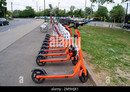 Slough, Berkshire, Großbritannien. 4. Mai 2022. Neurone e Roller am Burnham Bahnhof geparkt. Das von der Firma Neuron Mobility betriebene E-Scooter-Testmietprogramm in Slough wurde um weitere zwei Jahre verlängert. Die orangefarbenen Roller sind zwar beliebt, aber im Allgemeinen wurden E-Roller kritisiert, da einige Benutzer auf Gehwegen und Straßen mit ihnen zu Unfällen fahren. Kredit: Maureen McLean/Alamy Stockfoto