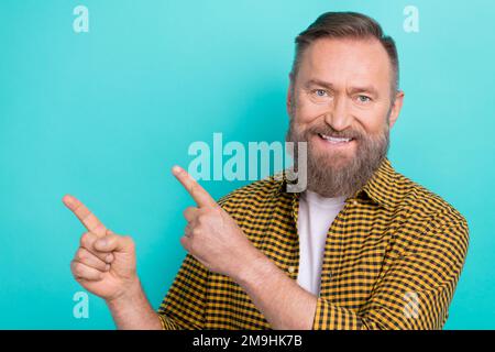 Fotoporträt eines Promoters im höheren Alter, der ein trendiges gelbes Hemd trägt, Zeigefinger leerer Raum, Neuheiten, isoliert auf aquamarinfarbenem Hintergrund Stockfoto