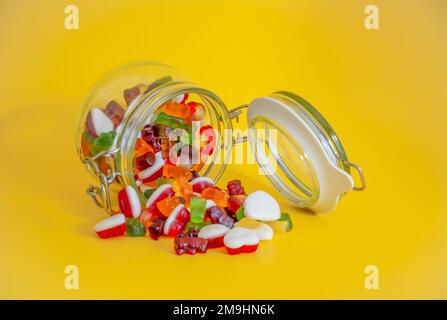 Süße Süßigkeiten Glasbehälter geöffnet mit süßen Süßigkeiten gegossen auf gelbem Tisch isoliert Stockfoto