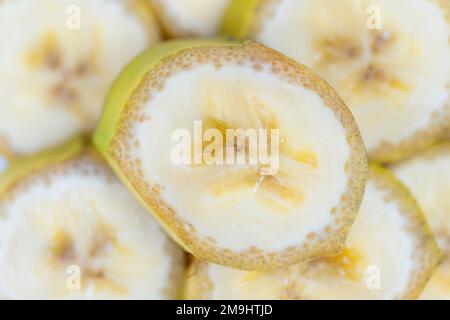 Bananenscheiben werden mit Haut in einer sehr nahen Makroaufnahme im Hintergrund geschnitten. Stockfoto