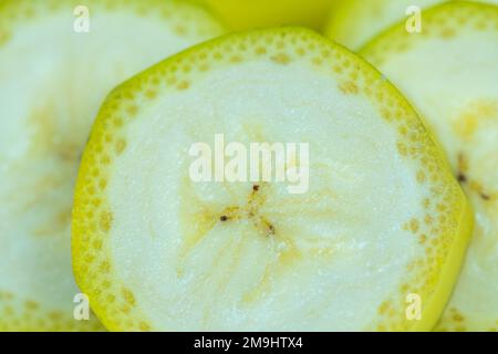 Bananenscheiben werden mit Haut in einer sehr nahen Makroaufnahme im Hintergrund geschnitten. Stockfoto