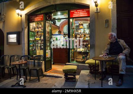 Nachtaufnahme eines alten Mannes, der ein Glas Wein auf der Terrasse der Arco Rosso Weinbar in Taormina, Sizilien trinkt Stockfoto