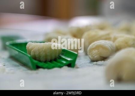 Eine Dame, die zum Mittagessen hausgemachte Gnocchi kocht. Die grüne Kröte, die dann hergestellt werden muss, befindet sich im Vordergrund Stockfoto