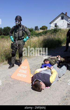 020715-F-5735S-045. [Complete] Szene Caption: Ein Officer des Pierce County, Washington (WA) Police Department, trägt nukleare, biologische, chemische (NBC) Ausrüstung und bewacht zwei verdächtige Terroristen während einer simulierten Chemiewaffenübung, die auf dem McChord Air Force Base (AFB), Fort Lewis, WA, während der Übung SEAHAWK 2002 durchgeführt wurde. Seahawk kombiniert aktive Dienst- und Reservekomponenten der US Air Force (USAF), der US Navy (USN), der US Coast Guard (USCG), des US Public Health Service, der Royal Canadian Armed Forces (RCAF), des Federal Bureau of Investigation (FBI) und des Federal Emergence Management Associat Stockfoto