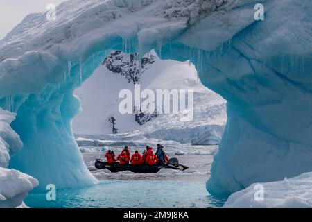 Touristen in einem Zodiac erkunden einen Eisbergbogen in Cierva Cove, einer Bucht entlang der Westküste von Graham Land, der Antarktischen Halbinsel und der Antarktis. Stockfoto