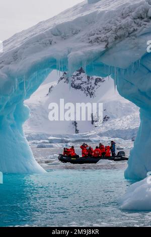 Touristen in einem Zodiac erkunden einen Eisbergbogen in Cierva Cove, einer Bucht entlang der Westküste von Graham Land, der Antarktischen Halbinsel und der Antarktis. Stockfoto