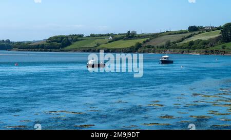 An einem Frühlingstag ankern zwei kleine Boote in Clonakilty Bay. Wunderschöne irische Küstenlandschaft. Klarer Himmel und blaues Wasser, Boote auf blauem Meer. Stockfoto