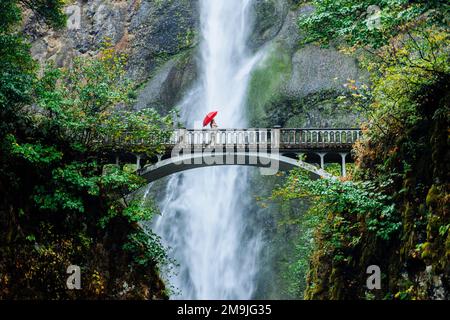 Frau mit Schirm auf der Brücke vor dem Wasserfall, Multnomah Falls, Columbia River Gorge, Oregon, USA Stockfoto