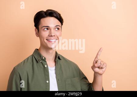 Portrait eines optimistischen, angenehmen Mannes mit braunem Haarschnitt, gekleidetem Khaki-Hemd, das den leeren Raum auf beigefarbenem Hintergrund zeigt Stockfoto