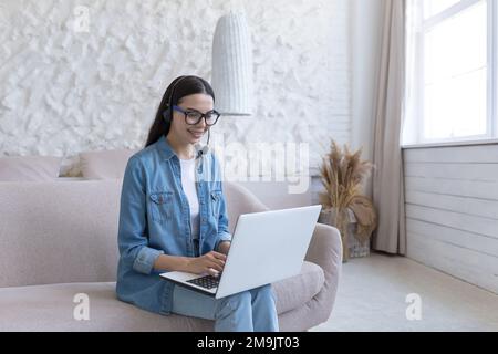 Fernunterricht. Porträt einer jungen, lächelnden Lehrerin mit Brille, die zu Hause auf dem Sofa sitzt und ein Notebook in der Hand hält. Arbeitet, unterrichtet von zu Hause aus online. Stockfoto