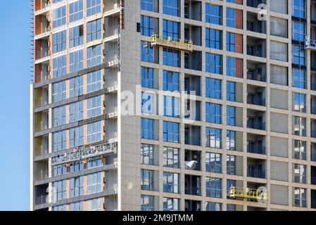 Der Bau eines mehrstöckigen Wohngebäudes, das Arbeitsteam an den Bauhalterungen, macht die dekorative Verkleidung der Fassade fertig. Stockfoto