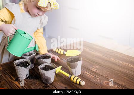 Wintervorbereitung für die Aussaat. Ein Mädchen gießt die Samen in Töpfen auf einem Holztisch mit gesäten Samen. Setzlinge für den Garten anbauen. Vegeta Stockfoto