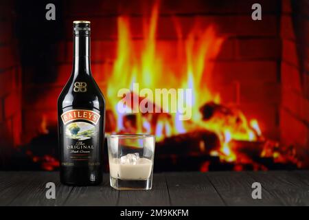 KIEW, UKRAINE - 4. MAI 2022 Baileys Original-Alkoholflasche auf Holztisch mit rotem Kamin im Hintergrund. Elite-Alkoholproduktion Stockfoto