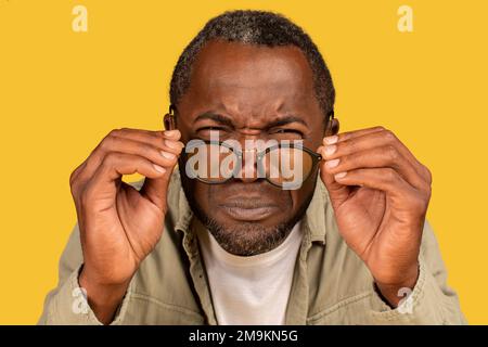 Konzentrierter afroamerikanischer Mann mittleren Alters, der Augen schielt, die Brille abnimmt, in die Kamera schaut Stockfoto