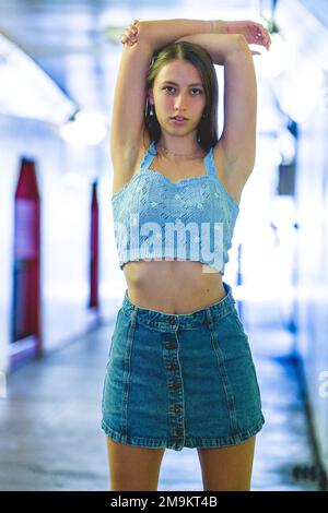 Half Body Portrait des modischen Teenage Girl in blauem Denim und Strickoberteil mit Bügeln über dem Kopf im Tunnel