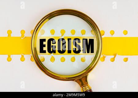 Zwischen zwei Blättern aus einem Notizbuch auf einem gelben Streifen mit der Inschrift - Egoismus, gibt es eine Lupe. Stockfoto